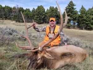 A man poses with the elk he took down during a guided hunt at Elk Ridge Outfitters