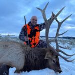 A man poses with the elk he took down during a guided hunt at Elk Ridge Outfitters