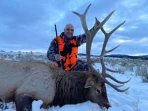 A man poses with the elk he took down during a guided hunt at Elk Ridge Outfitters