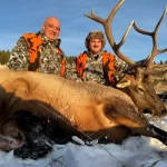 Two people stand behind an elk they successfully hunted