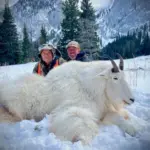 Two hunters pose with a mountain goat after a successful hunt