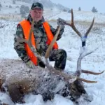 An Elk Ridge Outfitters guest poses with an elk he's taken down in snowy conditions.