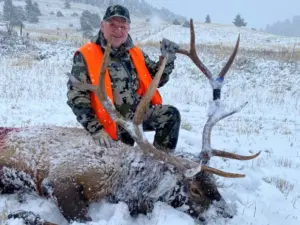 An Elk Ridge Outfitters guest poses with an elk he's taken down in snowy conditions.